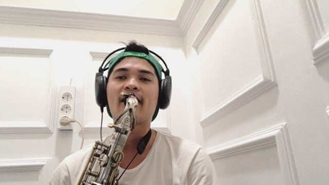 Erick Giri mengenakan topi dan headphone sedang memainkan saxophone